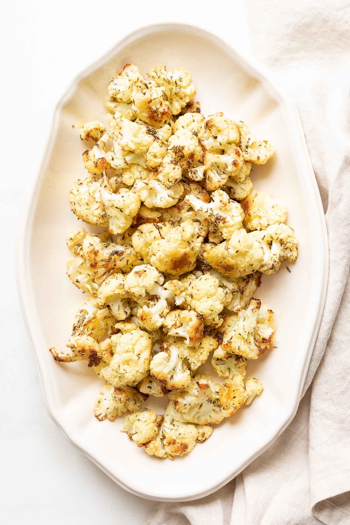 An oval white platter, filled with roasted cauliflower that is crispy and browned at the edges.