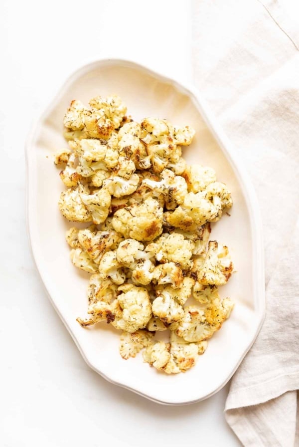 An oval white platter, filled with roasted cauliflower that is crispy and browned at the edges.