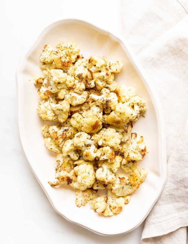 An oval white platter, filled with roasted cauliflower that is crispy and browned at the edges.