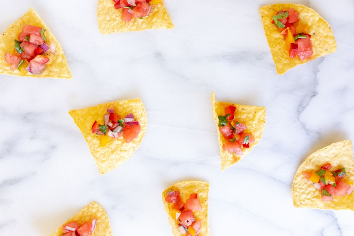 A marble countertop with tortilla chips scattered across, topped with fresh watermelon salsa.