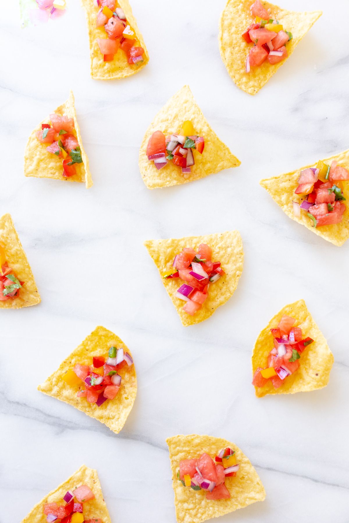 A marble countertop with tortilla chips scattered across, topped with fresh watermelon salsa.