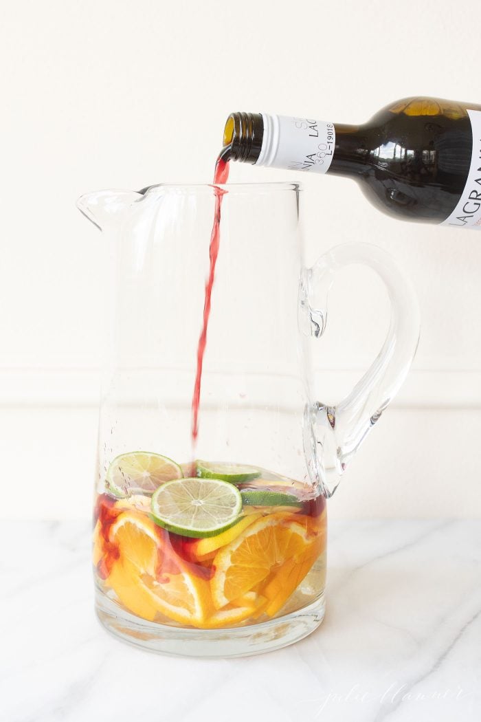 A pitcher filled with orange, lemon, and lime slices, with wine being poured in.