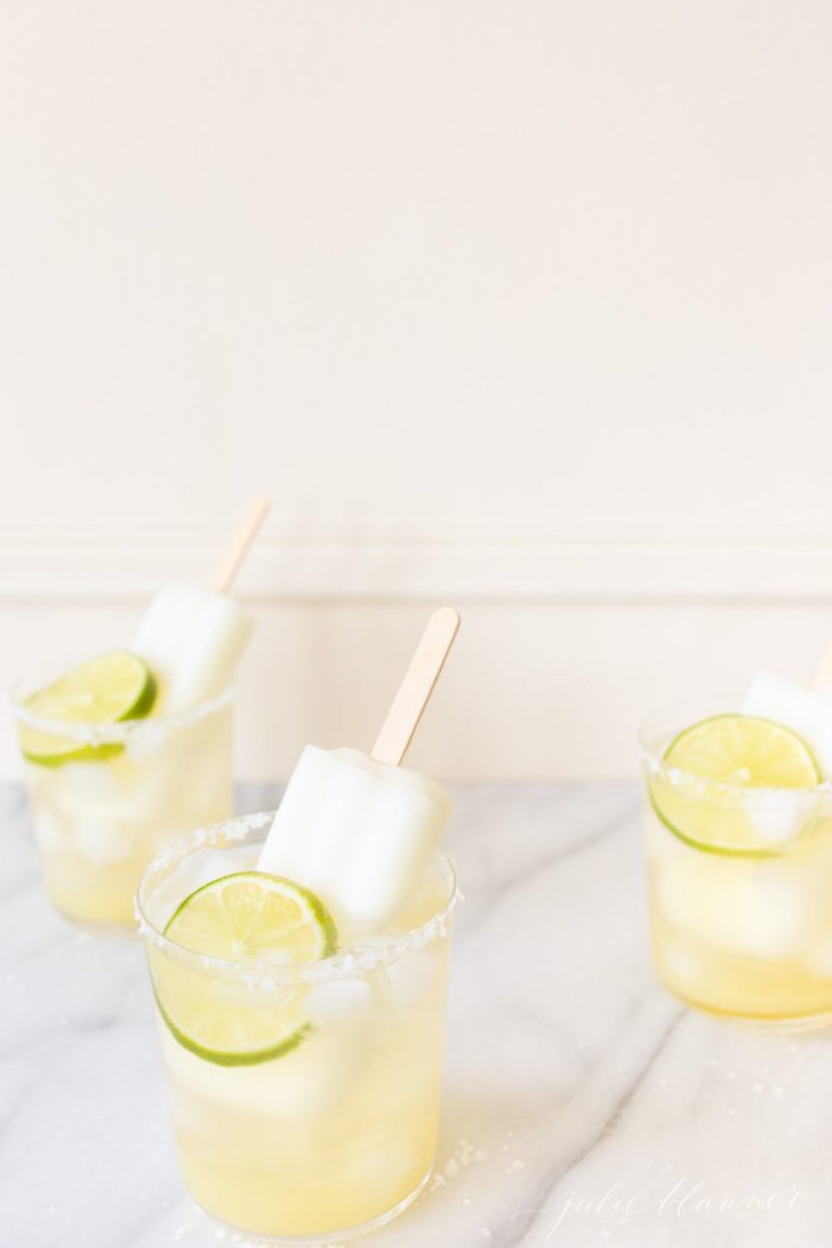 Three lime popsicle margaritas on a marble table.