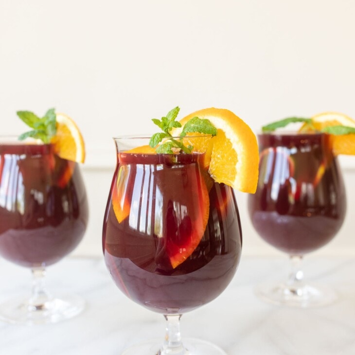 Three cups of sangria, garnished with a lemon slice and mint.