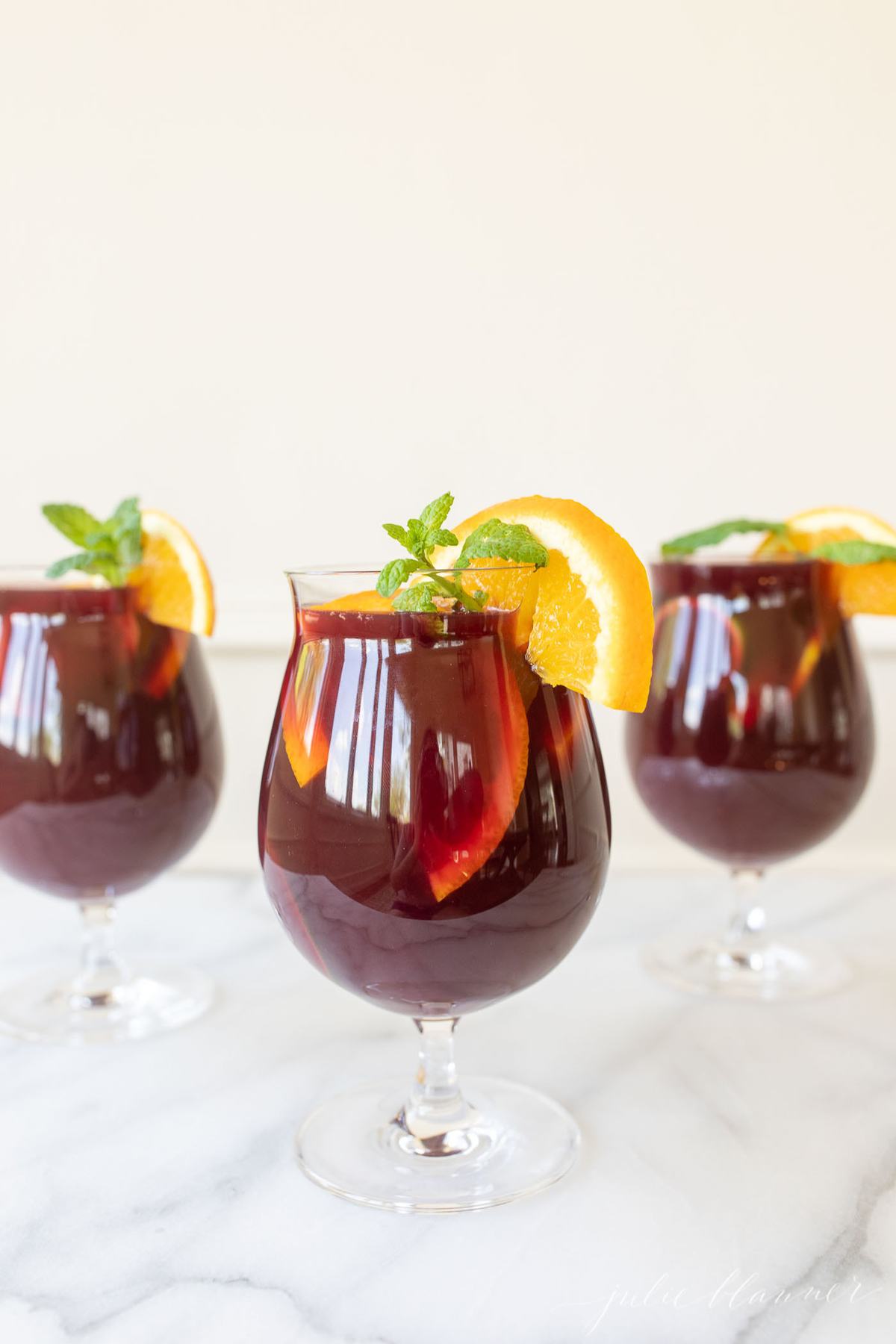 Three cups of sangria, garnished with a lemon slice and mint. 