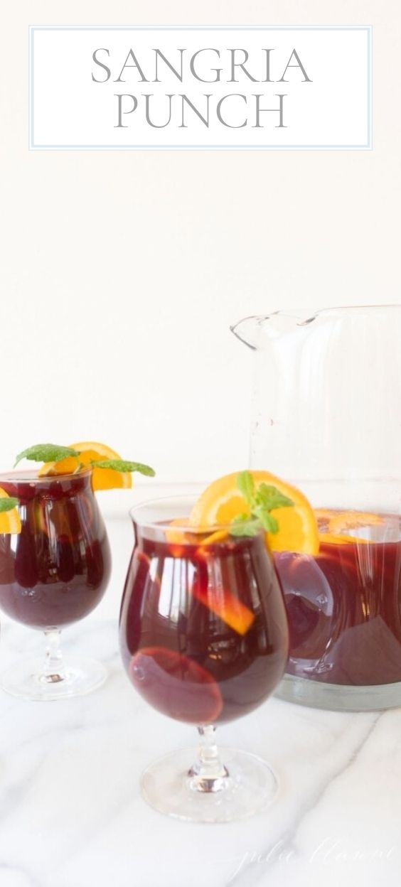 On a marble counter top, there is a glass pitcher and 3 drinkware glasses of Spanish Sangria Punch.