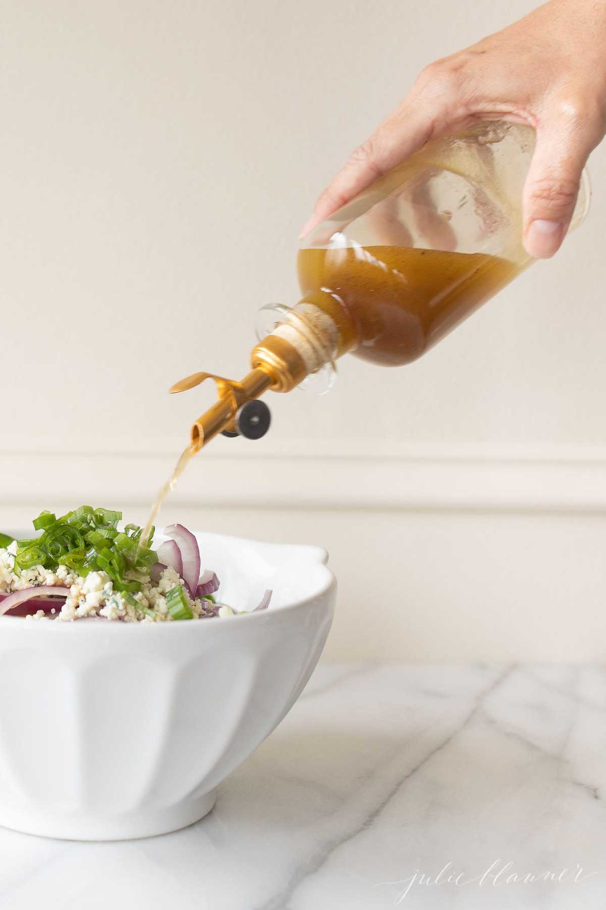 Bottle of Sherry Vinaigrette pouring over a salad in a white bowl.