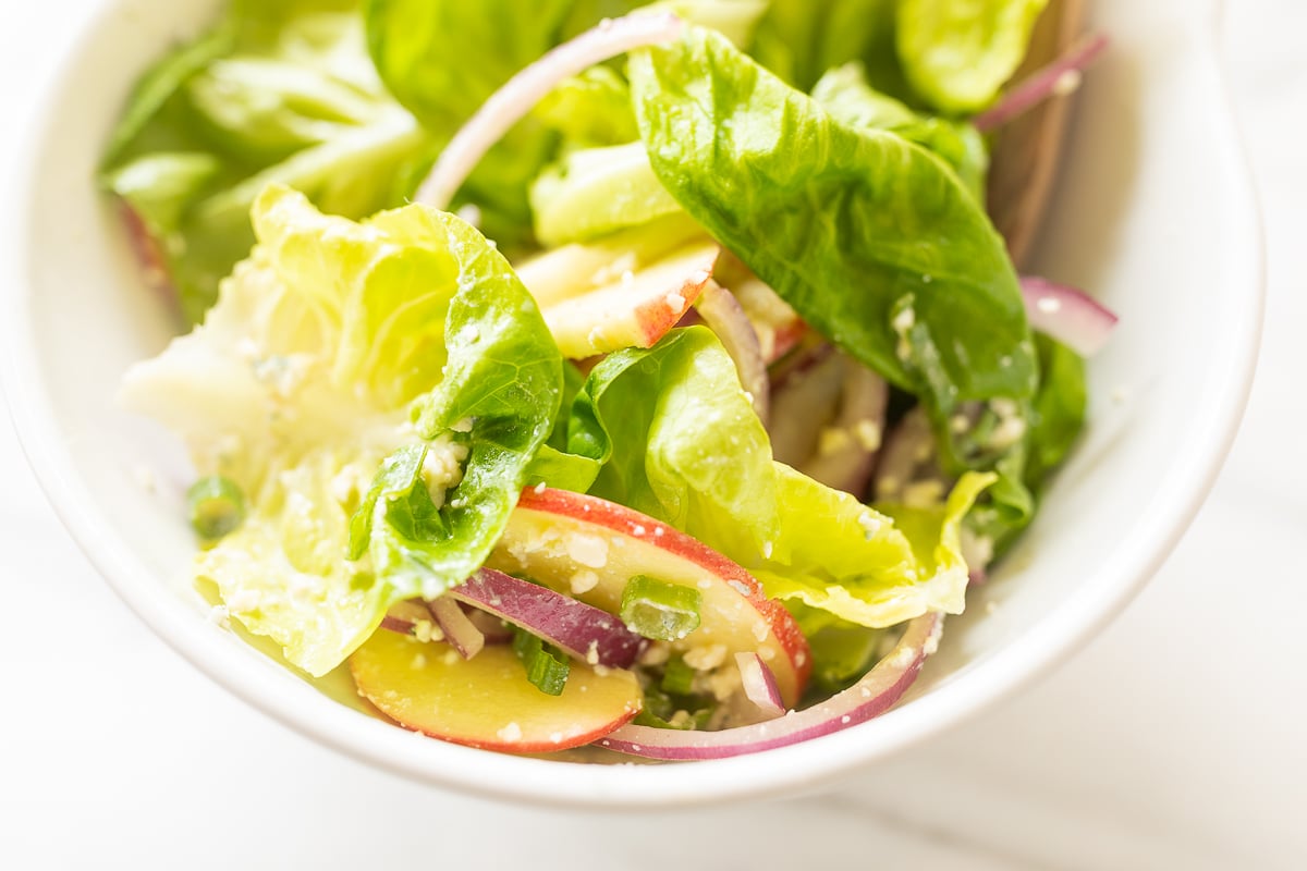 A white bowl full of homemade apple salad, with wooden serving spoons.