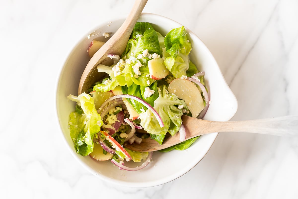 A white bowl full of homemade apple salad, with wooden serving spoons.