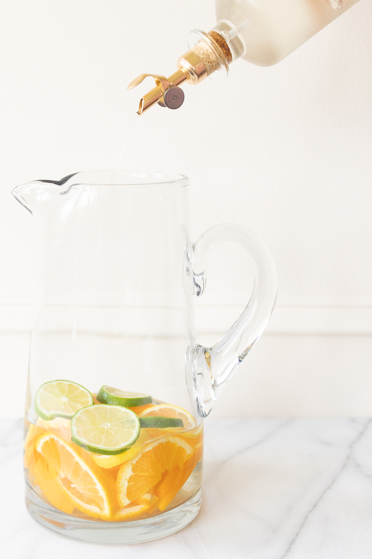 A glass pitcher full of fruit for red sangria, simple syrup being poured over the top.