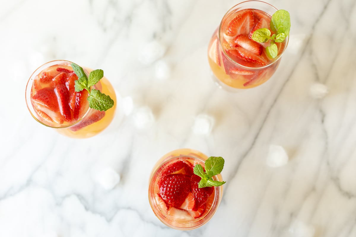 Three glasses of Moscato sangria garnished with strawberries, peaches and mint.