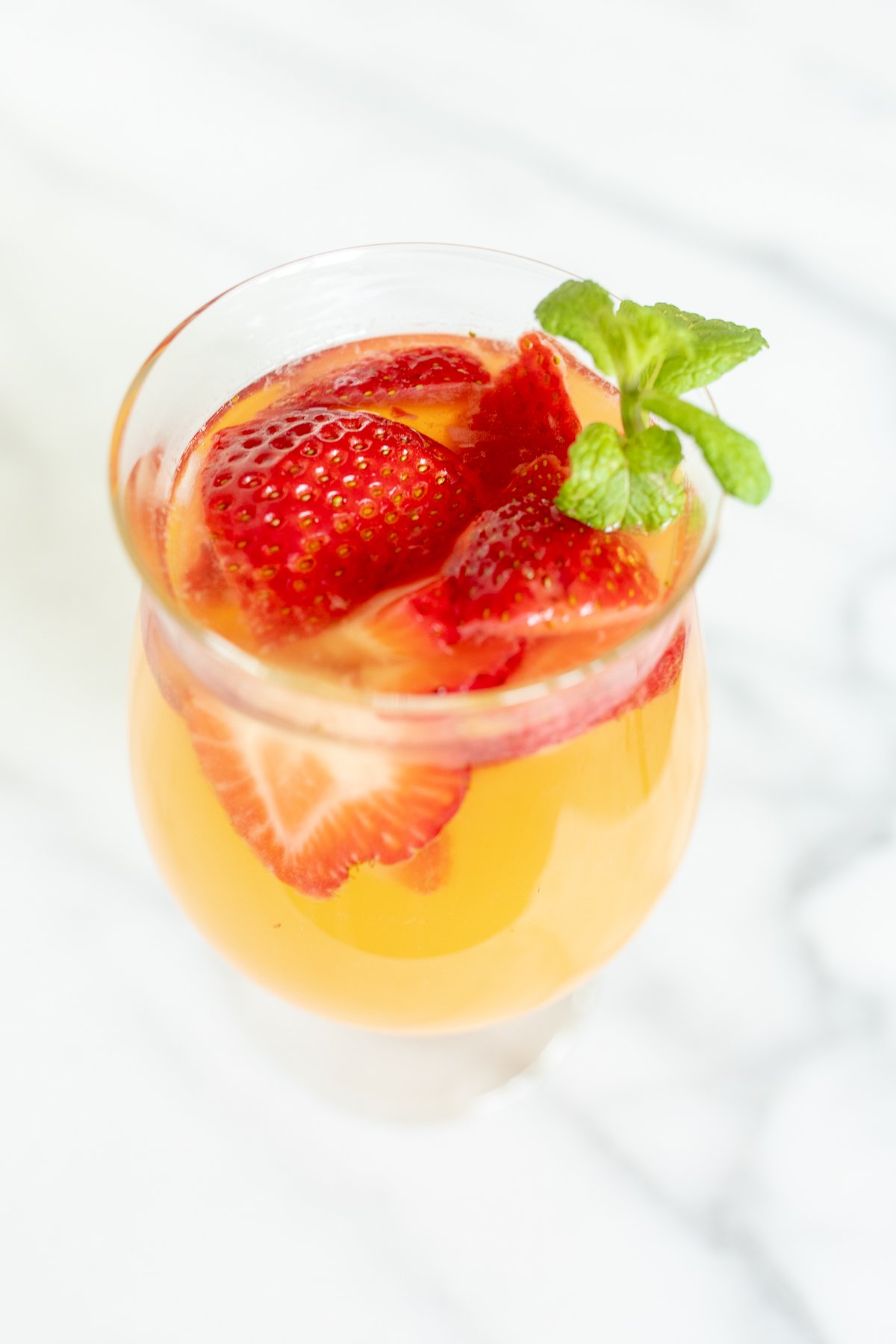 A glass of Moscato sangria garnished with strawberries, peaches and mint.