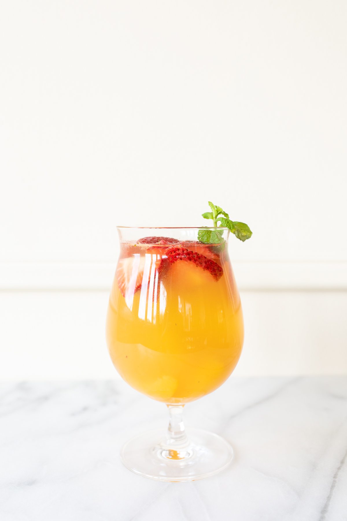 A glass of Moscato sangria garnished with strawberries, peaches and mint.