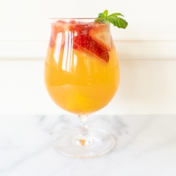 A glass of Moscato sangria garnished with strawberries, peaches and mint.