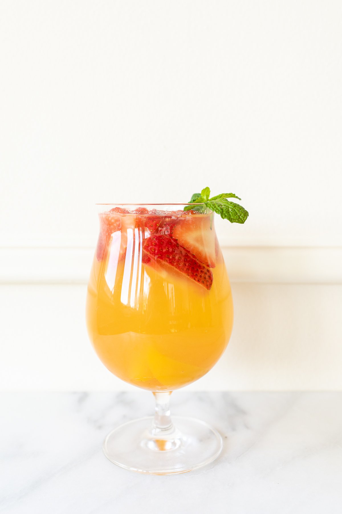 A glass of Moscato sangria garnished with strawberries, peaches and mint. 