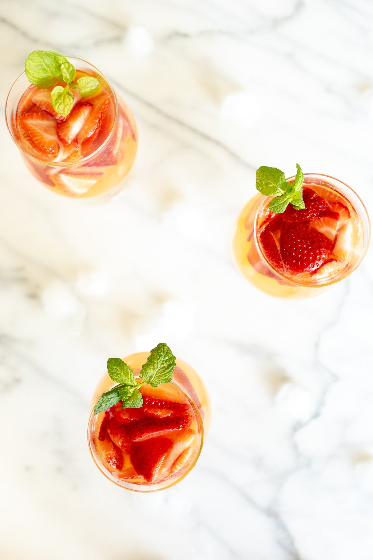 Three glasses of Moscato sangria garnished with strawberries, peaches and mint.