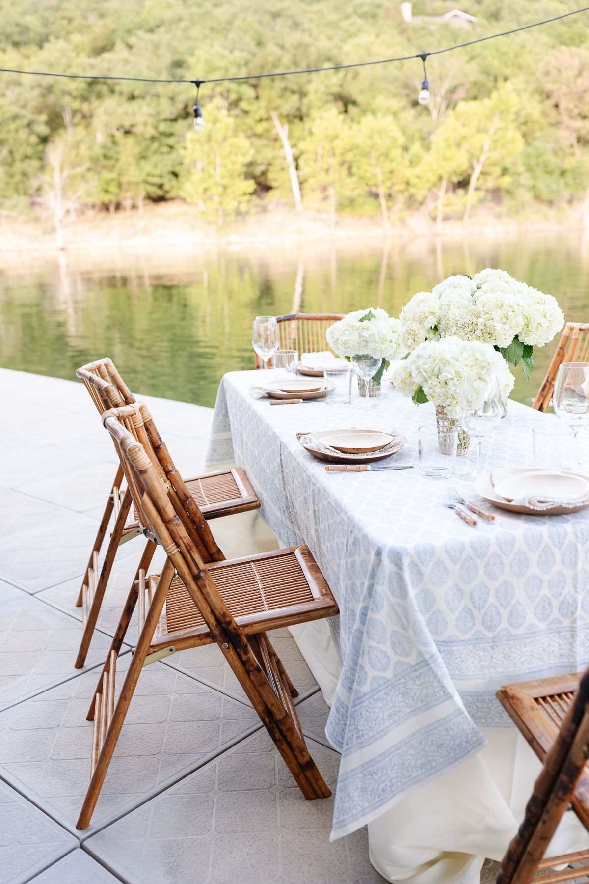 A mother's day brunch set up with white flowers and bamboo chairs on a dock at a lake