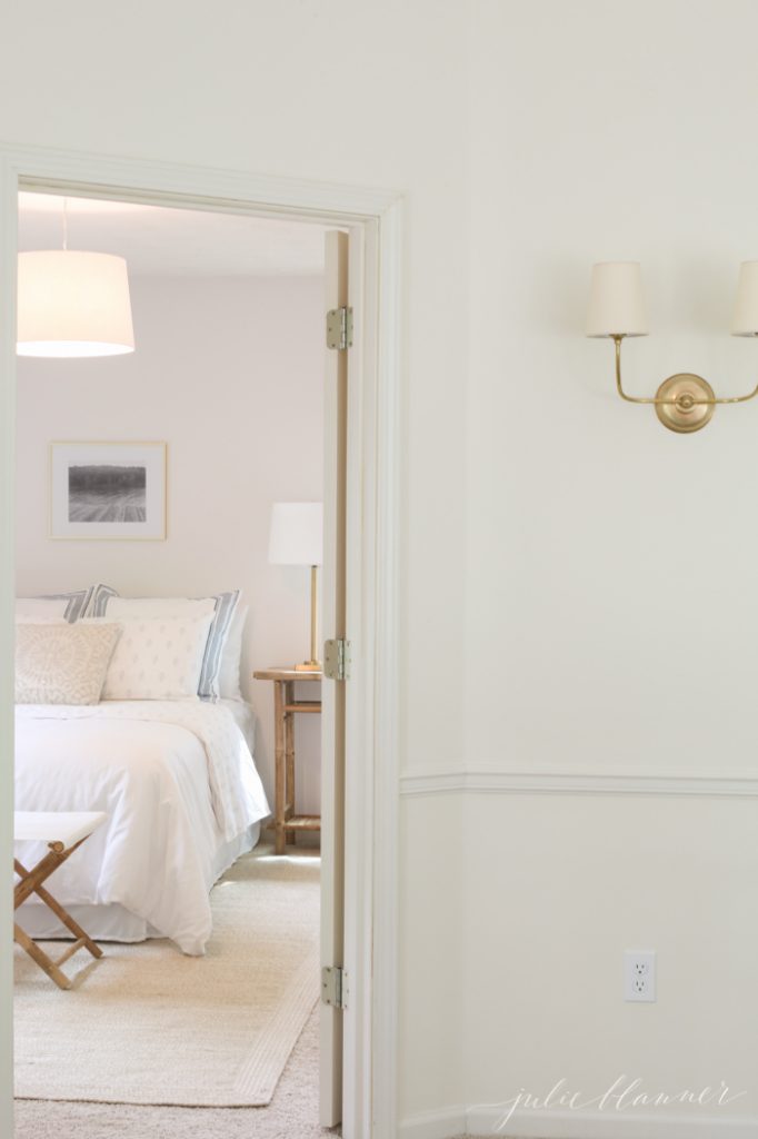 A hallway looking into a white guest bedroom with white bedding.