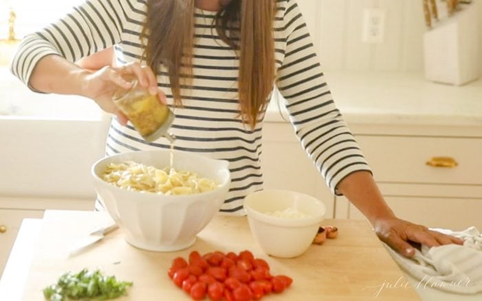 pouring pasta salad dressing onto pasta salad