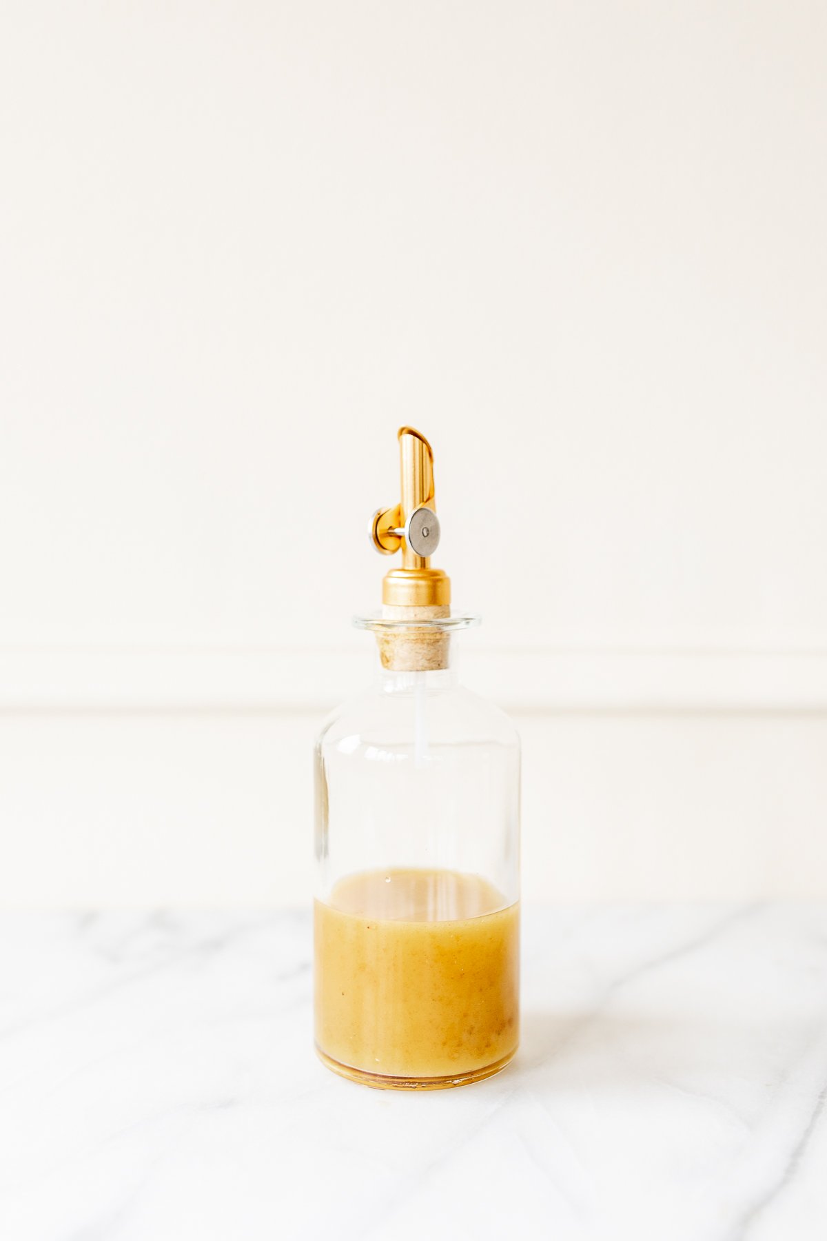 Una botella de vidrio con tapón dorado sobre una encimera de mármol, llena de vinagreta de jerez.