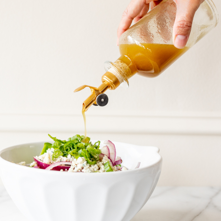 A bottle of dressing being poured over a salad in a white bowl.