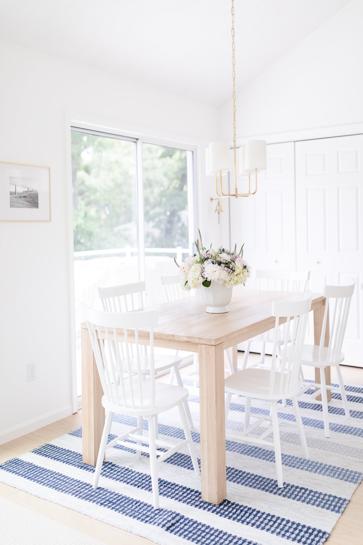 A small dining room table with white chairs and a vase of flowers.