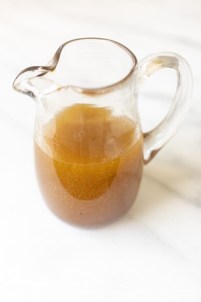 Balsamic vinaigrette in a clear pitcher on a marble surface.