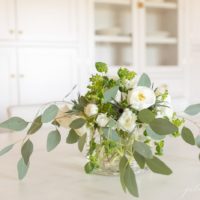 A floral bouquet with white blooms and loose whispy greenery on a white countertop.