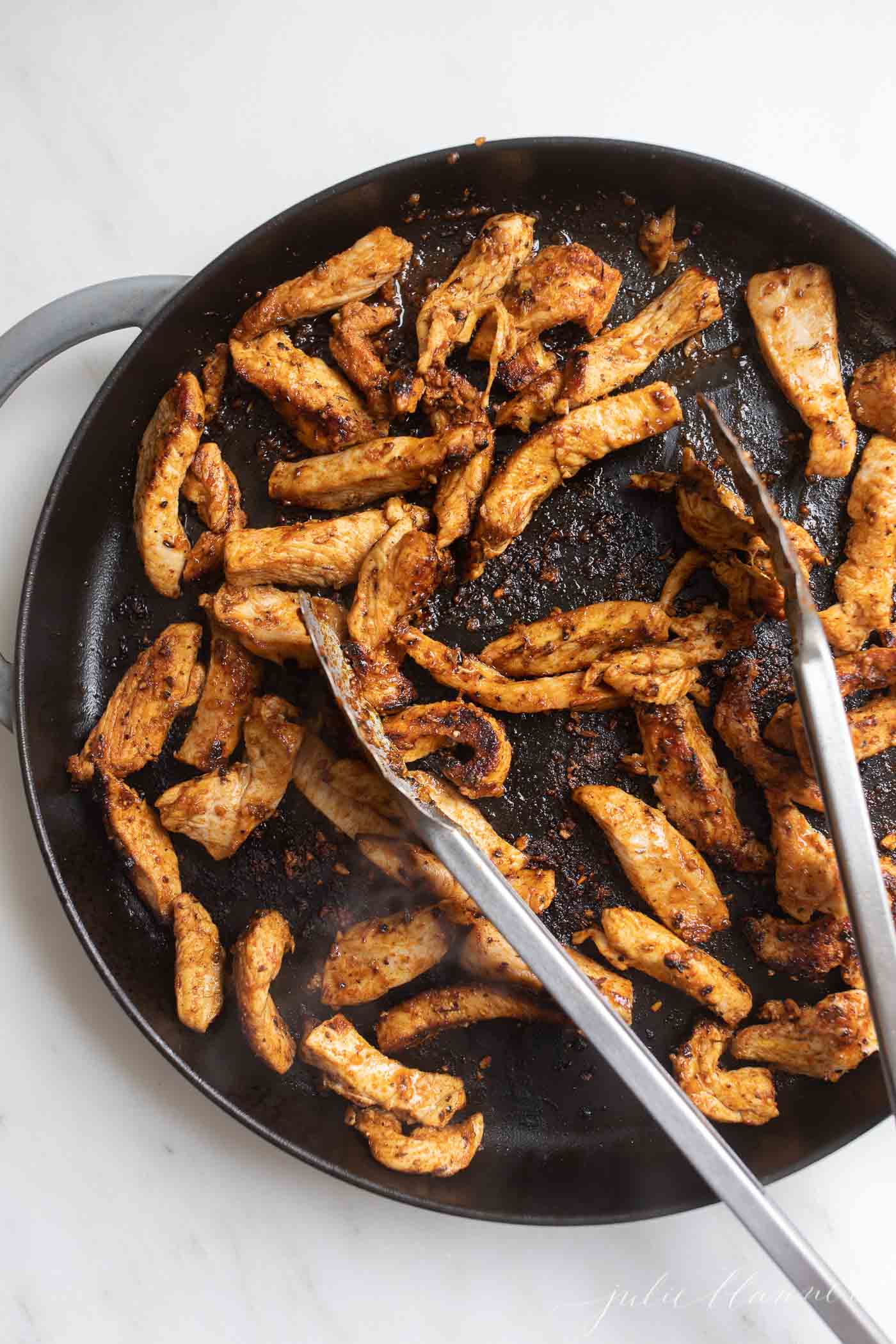 cajun spiced chicken in a skillet with tongs