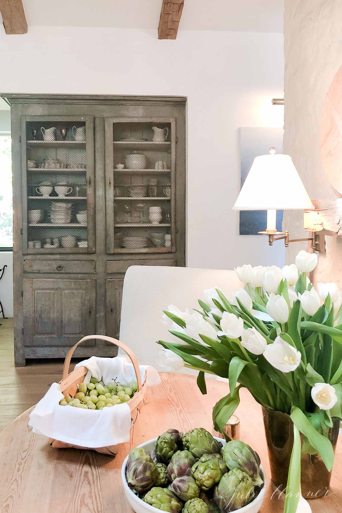 Old farmhouse cabinet filled with collectibles, flowers in foreground.