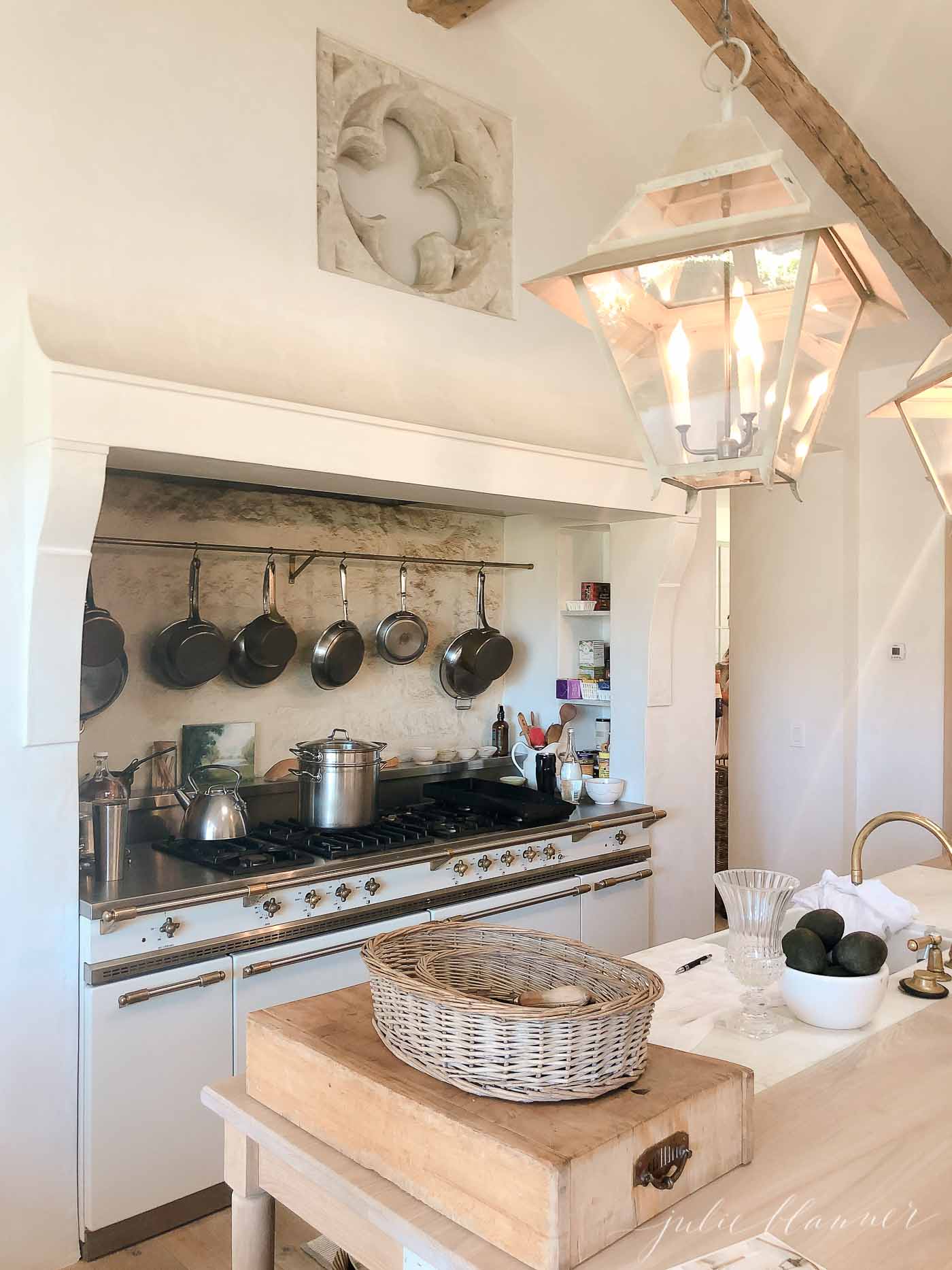 Utilitarian French kitchen with Lacanche range and collection of pots hanging above.