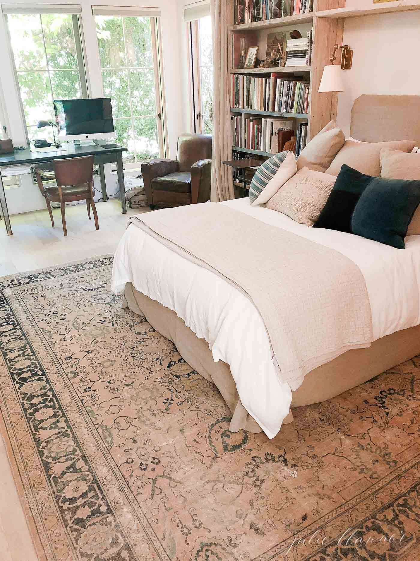 European farmhouse inspired bedroom with antique rug, bookshelves and linen bedding.