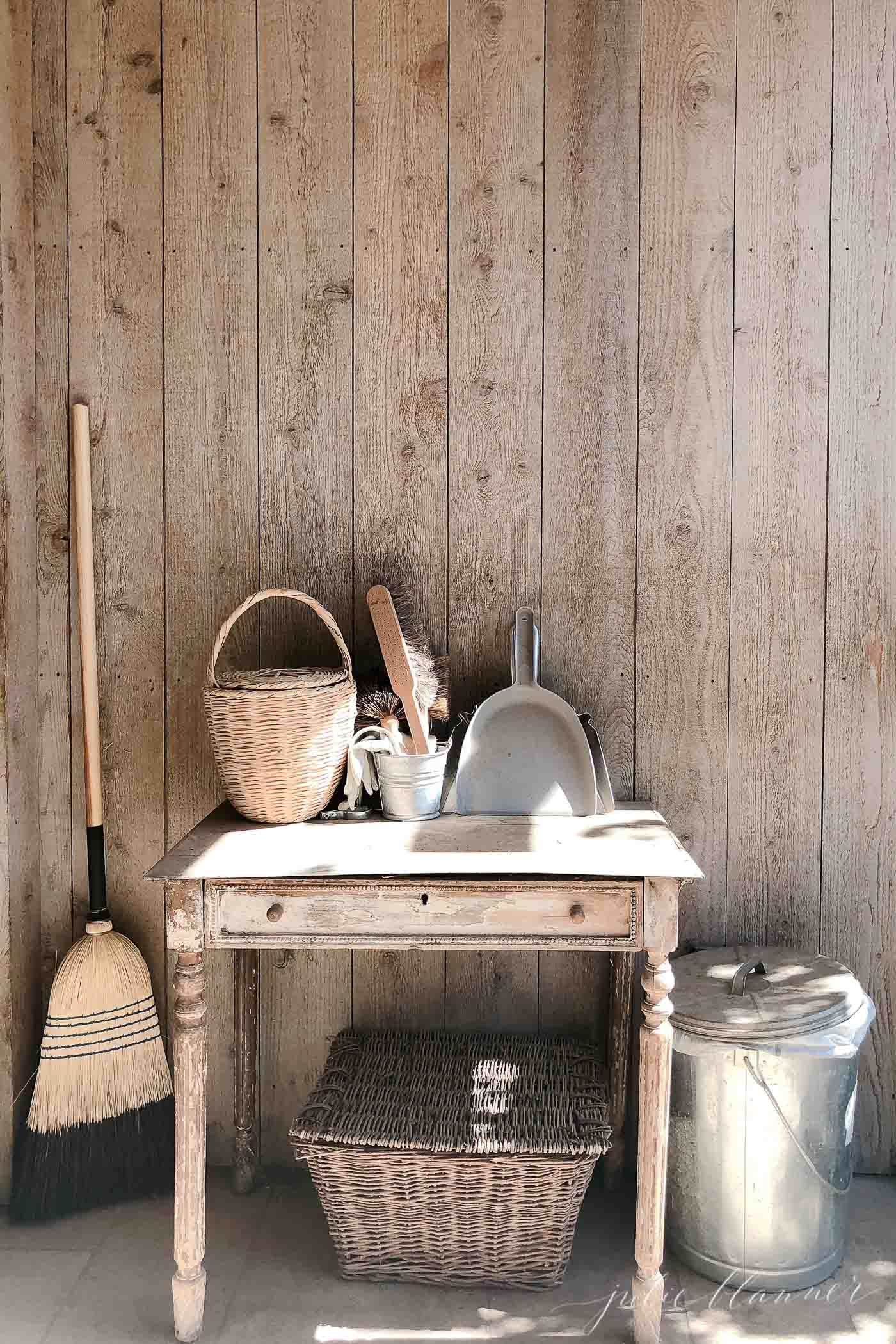 A raw wood wall with a simple wood table, piled with rustic cleaning supplies. 