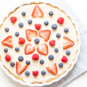 A freshly prepared fruit pizza with creamy filling, garnished with strawberries, blueberries, and raspberries.