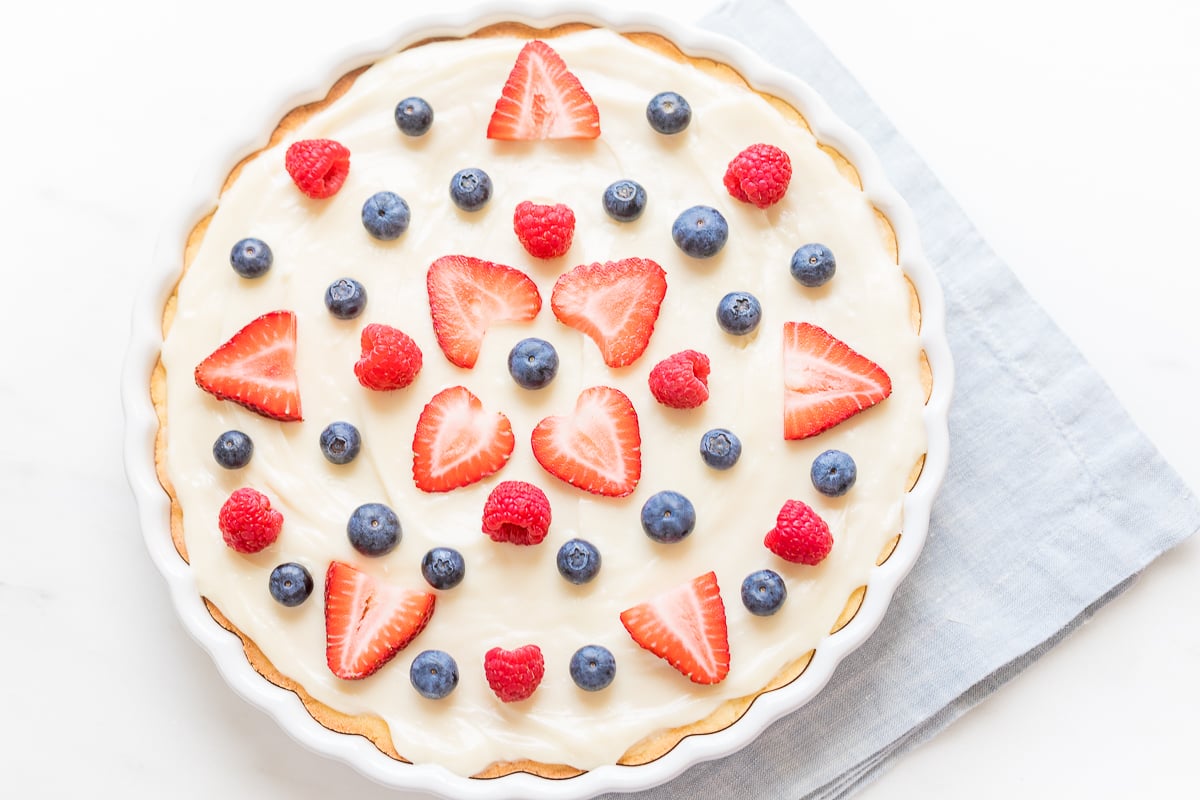 A vanilla tart topped with fresh strawberries and blueberries following an easy fruit pizza recipe.