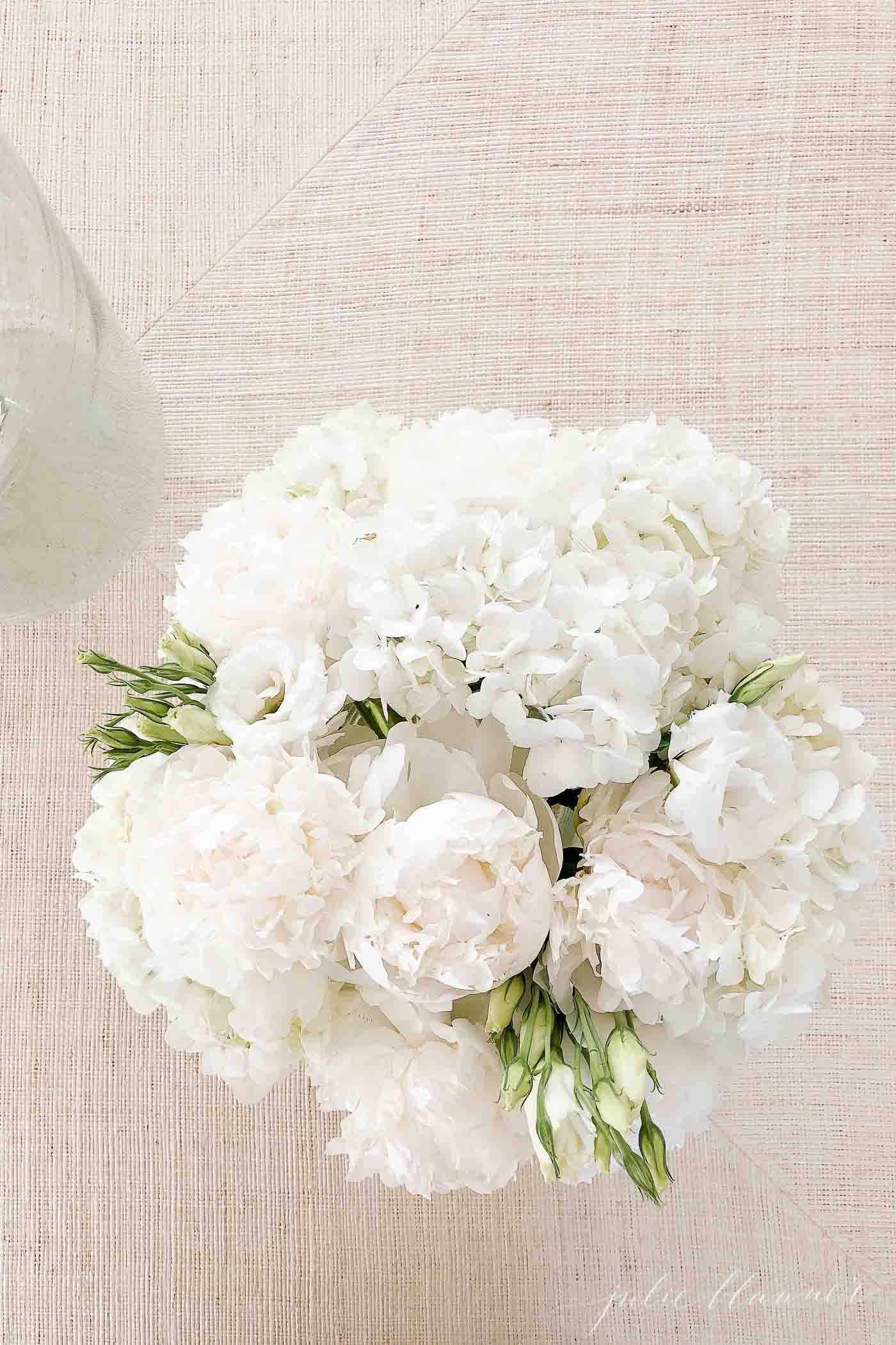 Florist arrangement of white hydrangea and peonies on a neutral rattan coffee table.