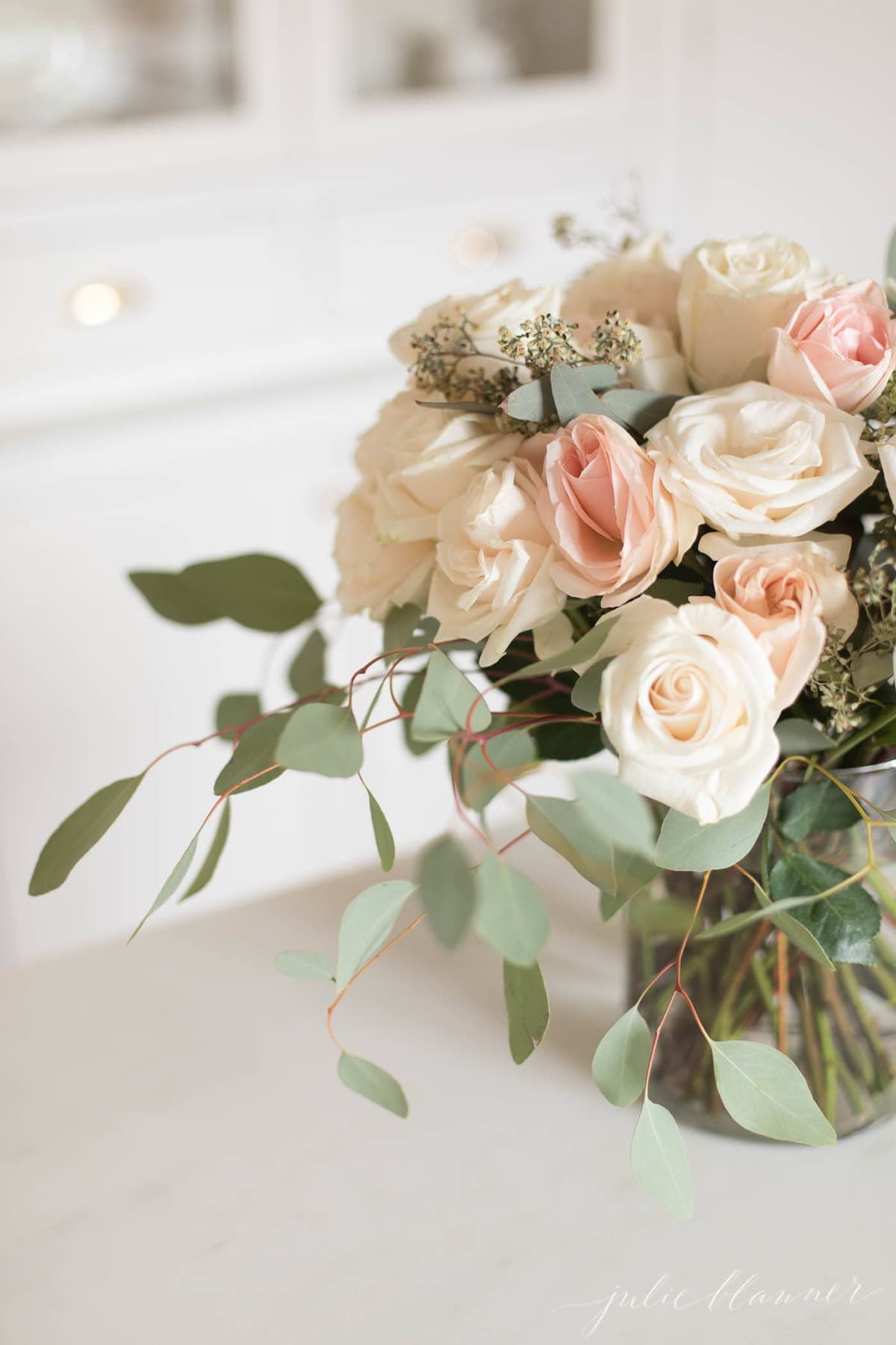 pastel peach roses and soft gray eucalyptus foliage floral design in a white kitchen.