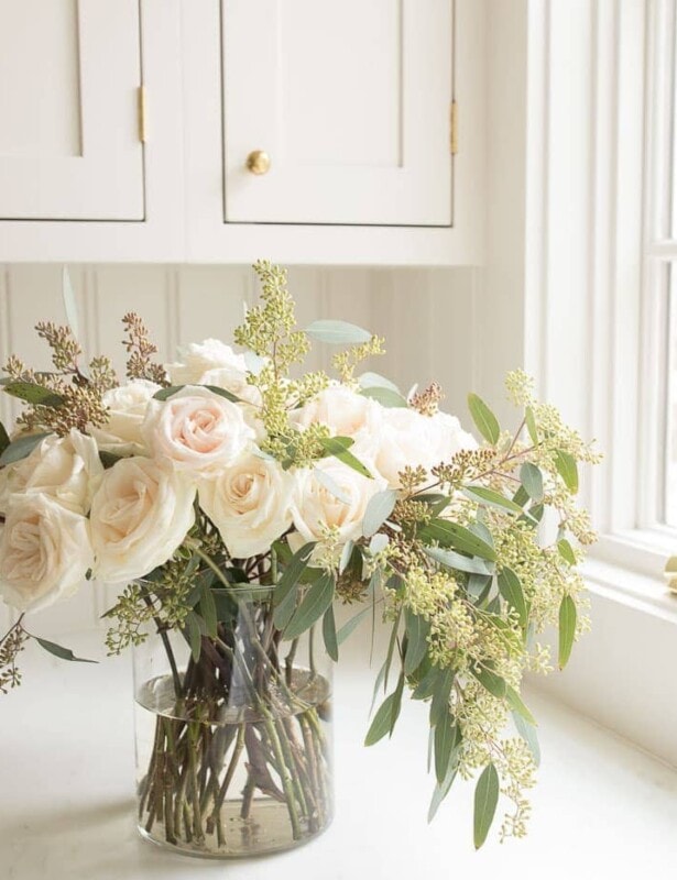 Cream kitchen backdrop with a simple clear cylinder vase filled with roses and eucalytpus.