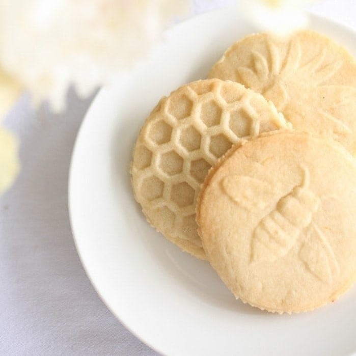 A white plate of lemon shortbread cookies stamped in bee themed designs