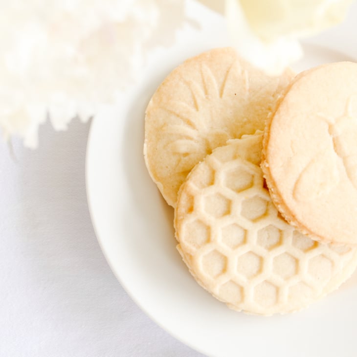 lemon shortbread cookies stamped with flowers, bees and beehives on a white plate