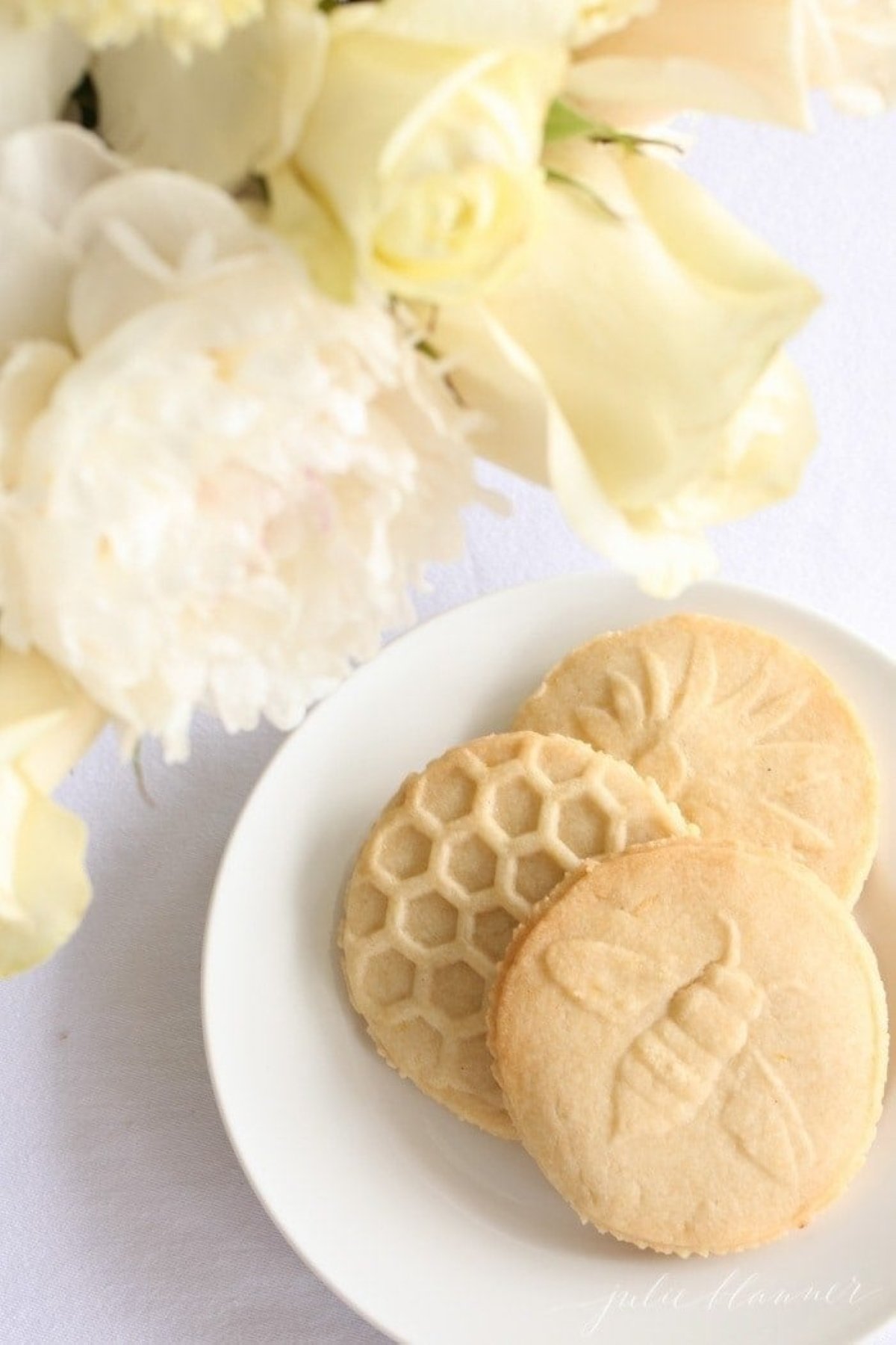 Lemon shortbread cookies on a white plate with fresh flowers nearby