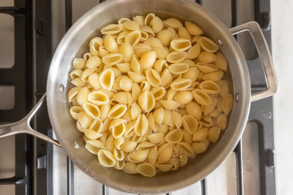A stainless steel pan on a stove top with pasta shells.