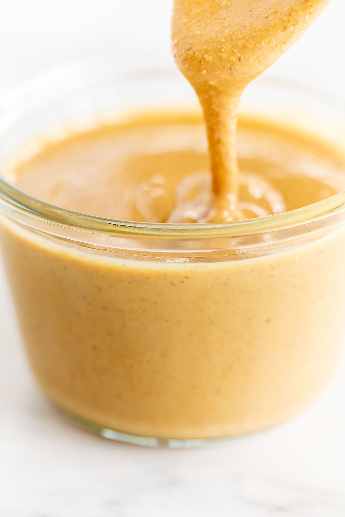 A glass jar full of homemade peanut butter on a marble surface