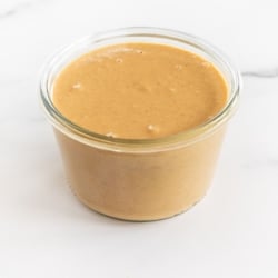 A glass jar full of homemade peanut butter on a marble surface