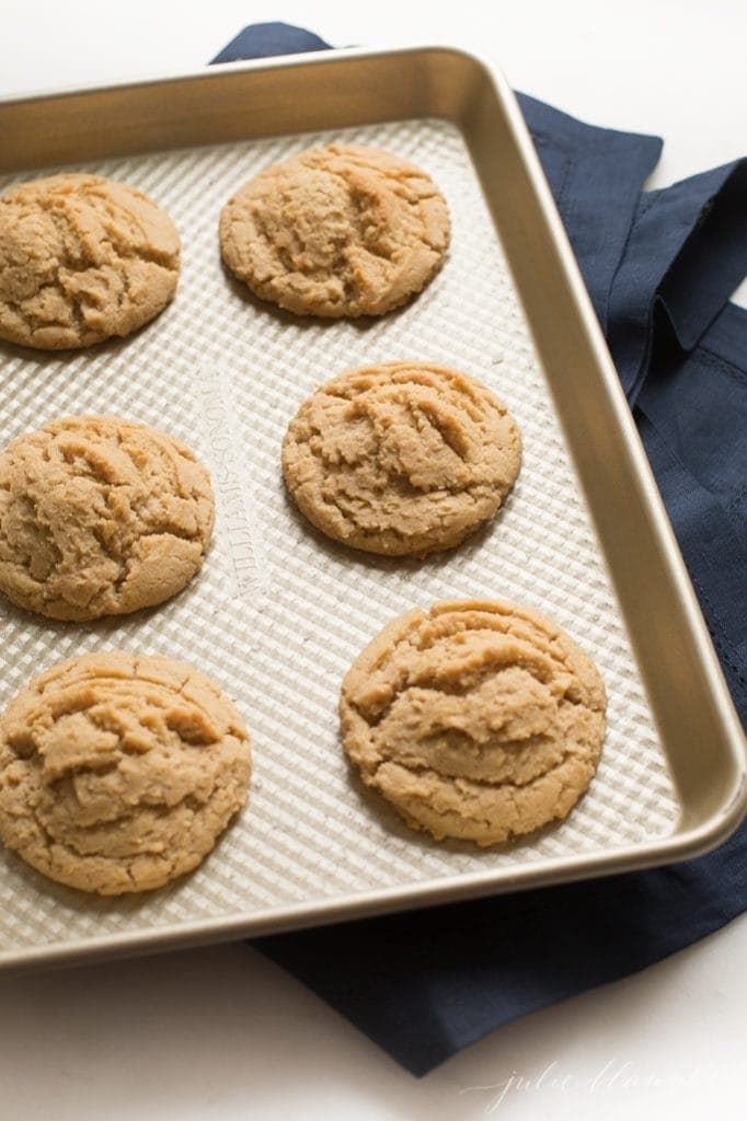 A gold baking tray with peanut butter cookies stuffed with Snickers bites.