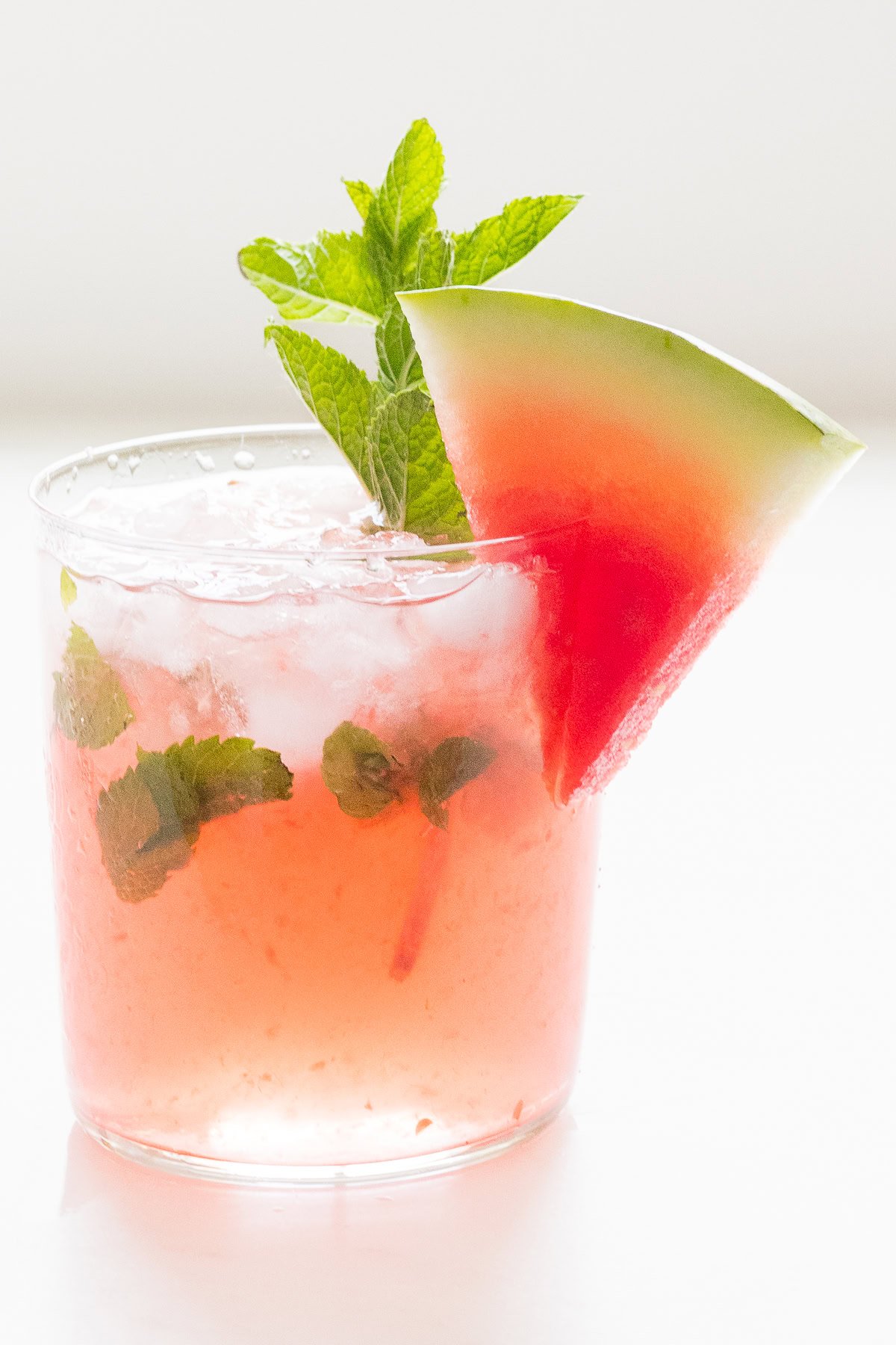 A refreshing watermelon mojito in a glass, garnished with a slice of watermelon and mint leaves, on a white background.