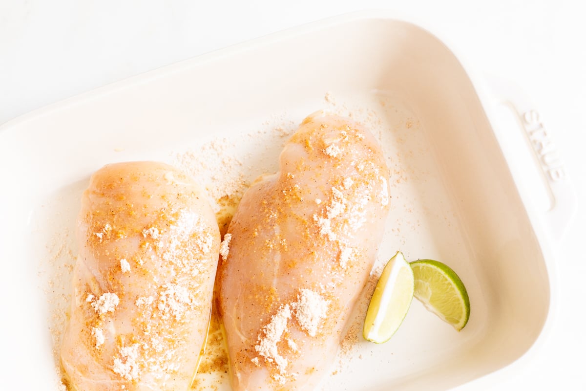 Chicken breasts in a white baking dish before baking.