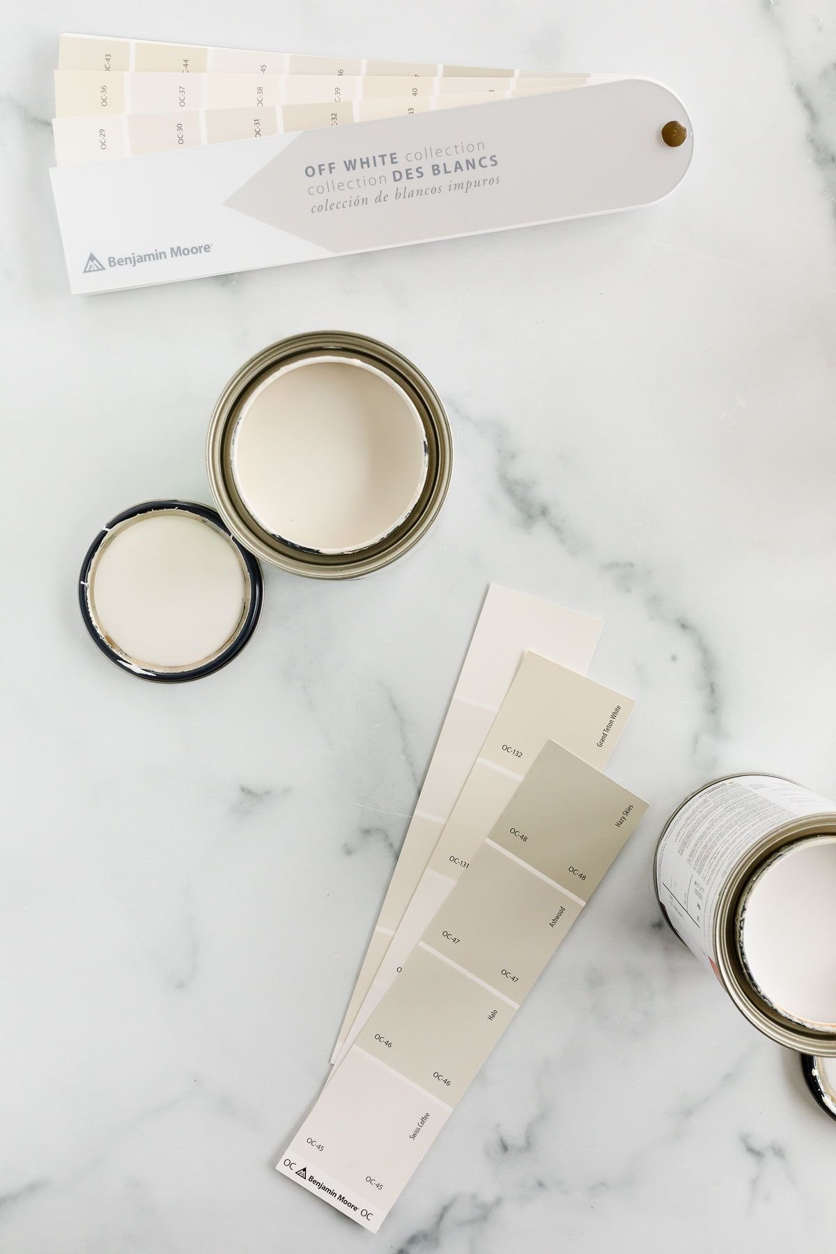 A marble countertop with paint swatches and small cans of open cream paint colors.