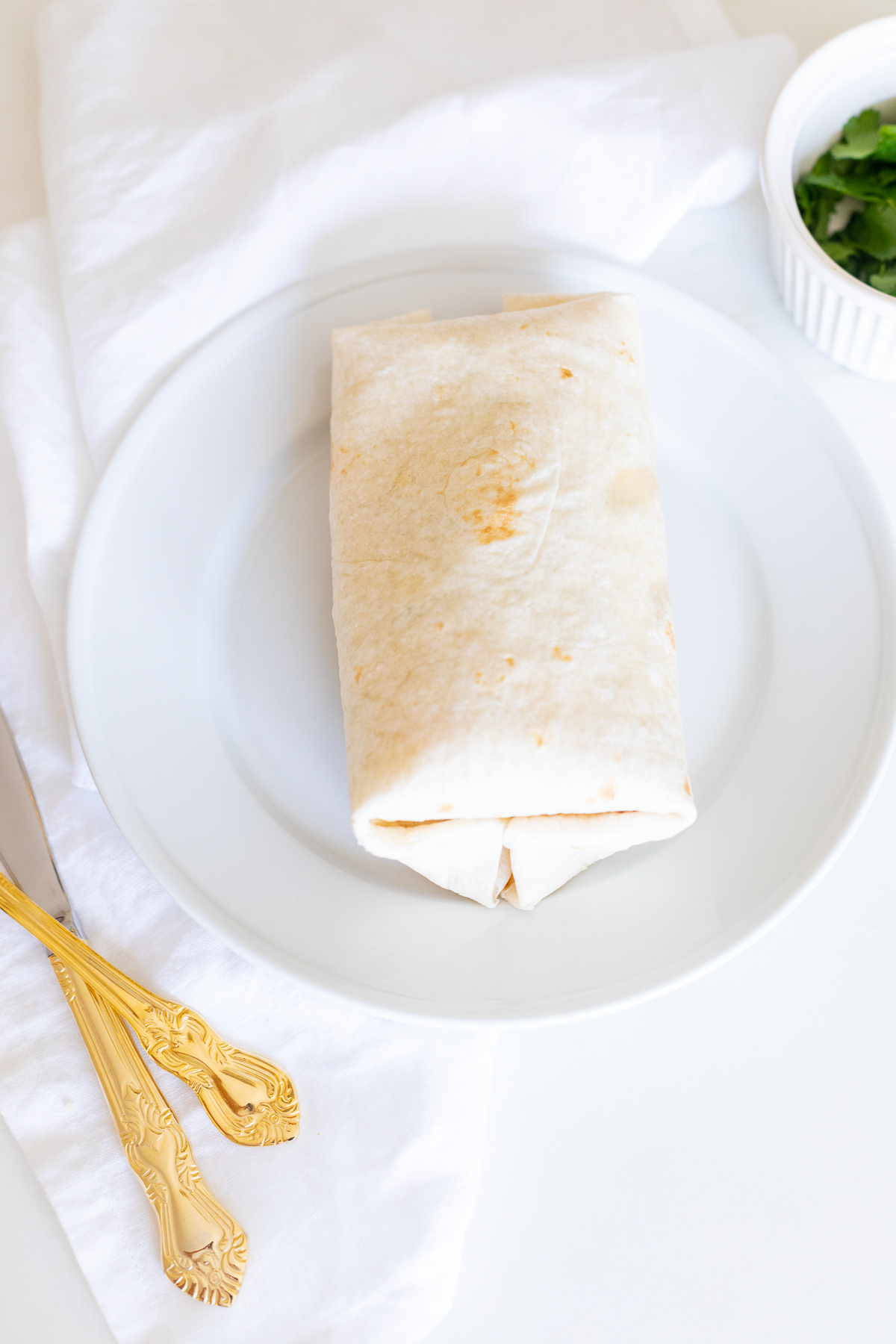 A chicken wrap on a white plate with gold silverware.