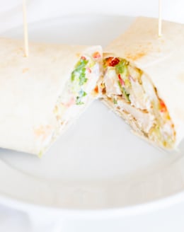 A chicken wrap recipe on a white plate, cut in half.